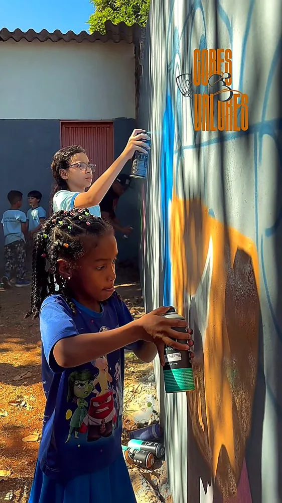Duas crianças pintando um muro com spray, em evento do projeto Cores e Valores