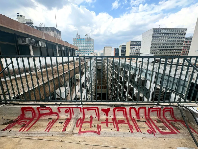 Vista de telhados e prédios da cidade a partir de um terraço, com tag em vermelho no parapeito